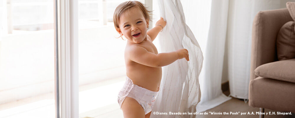 Bebé jugando con la cortina y sonriendo.